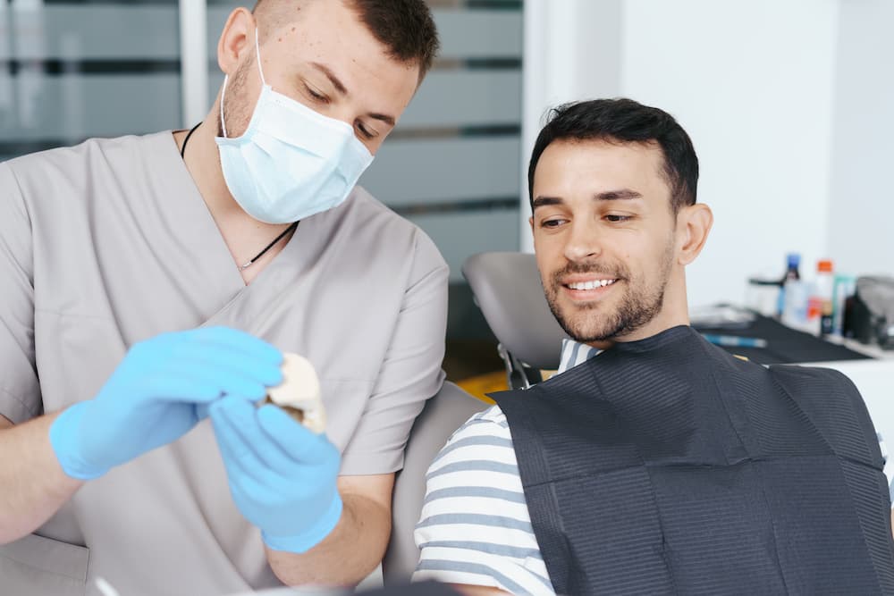 male dentist showing patient the artificial dentur W74LN42 1